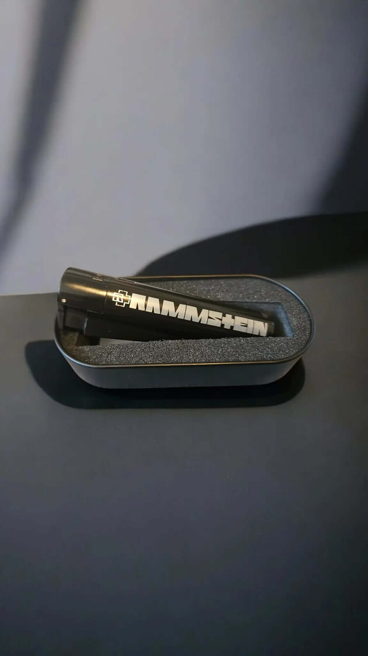 Rammstein Feuerzeug in schwarzem Etui auf dunklem Hintergrund.