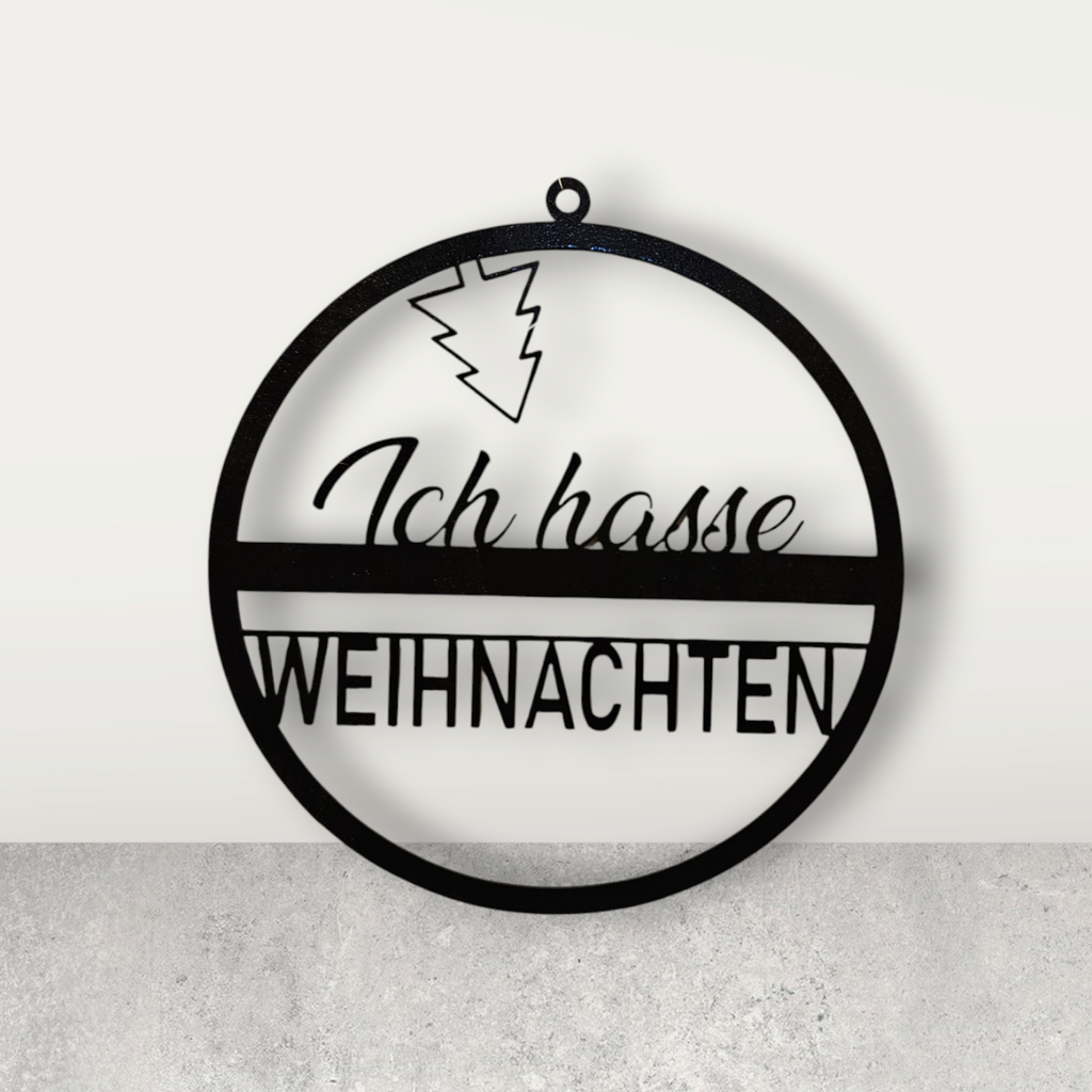 Eine kreisförmige Türdekoration, in der Mitte der Text "Ich hasse Weihnachten" in 2 verschiedenen Schriftarten, oben ist ein Weihnachtsbaum kopüber angebracht". Schwarz
